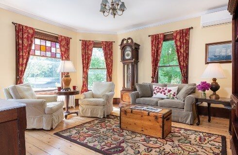 Cozy sitting room with couch, two chairs, coffee table chest and windows with stained glass