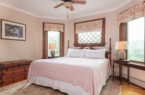 Elegant Victorian style bedroom with king bed, large windows with floral valences and side tables with lamps