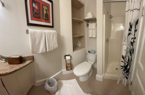 Bathroom with sink, mirror, toilet by a built in shelf and stand up shower with a black and white curtain