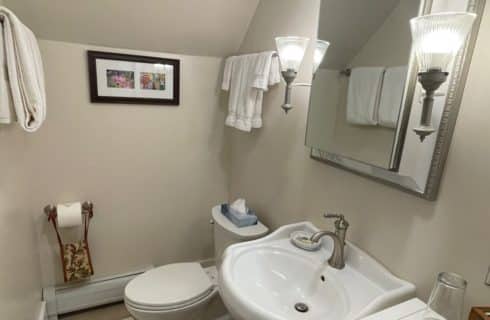 Bathroom with pedestal sink, toilet, mirror with lamp sconces and hanging white towels