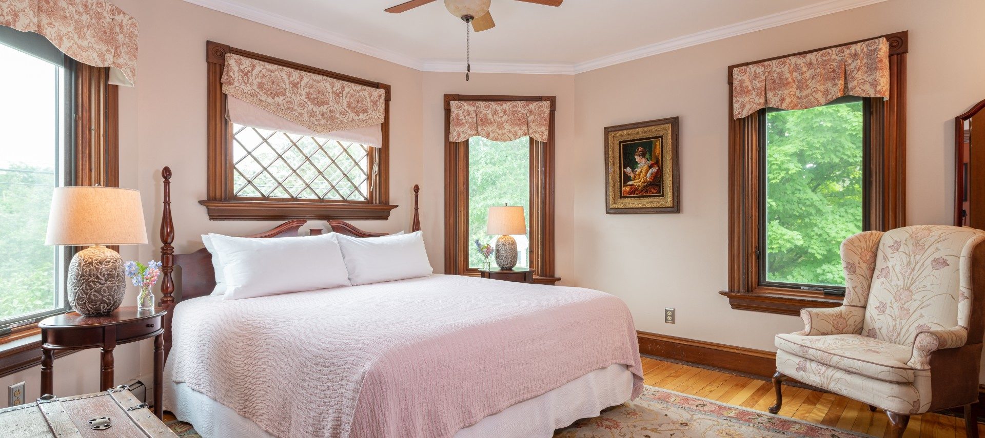 Elegant bedroom with king bed, wingback sitting chair. and four bright windows with floral valences