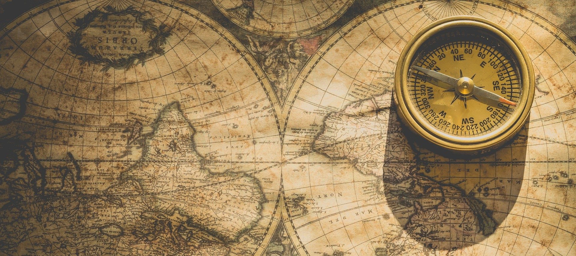An old world map and small round golden compass sitting on a table
