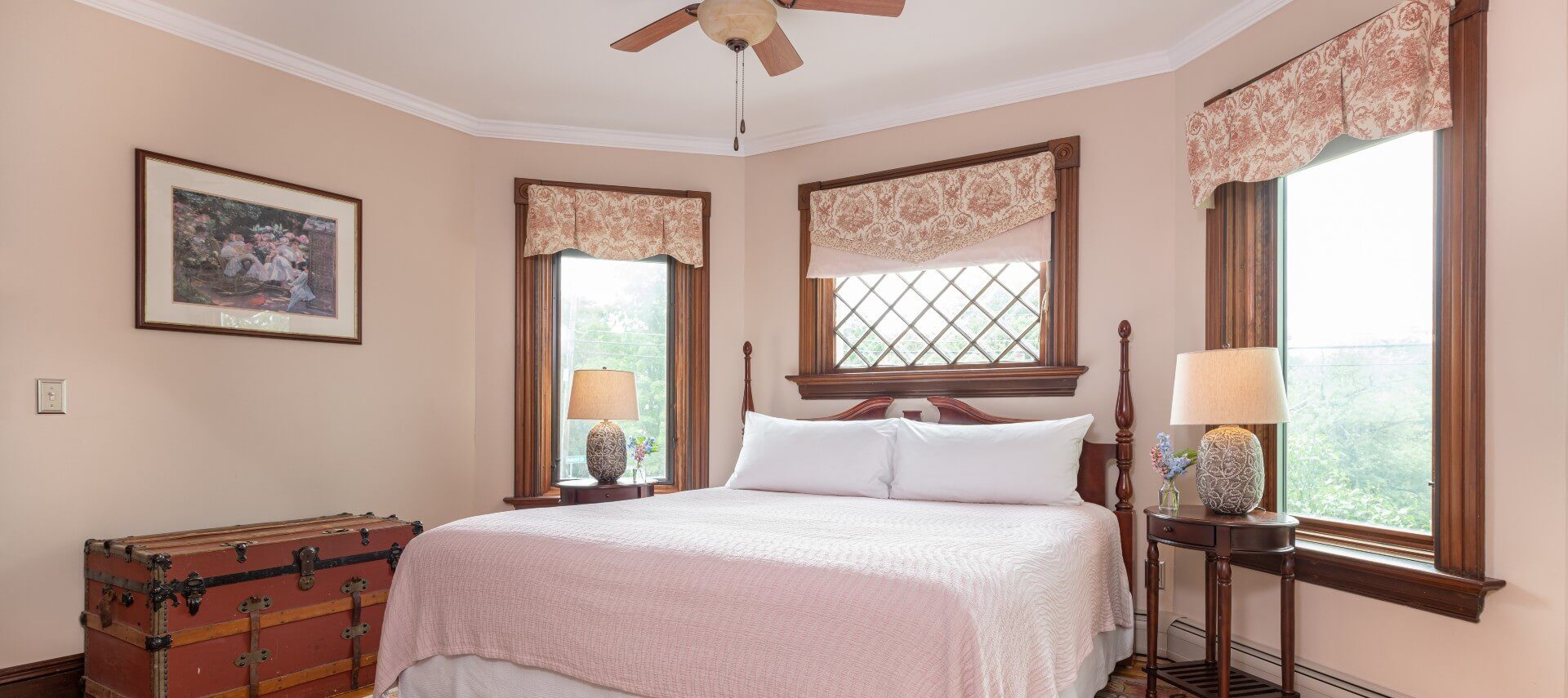 Elegant and bright bedroom with a king bed, side tables with lamps and bright windows with floral valences