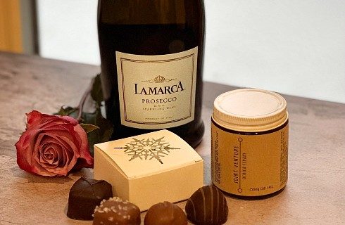 A bottle of wine with a single red rose and box with four chocolates